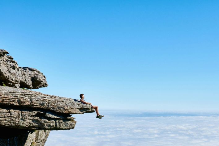 A person sits on a cliff edge enjoying a breathtaking view of the ocean and city below.